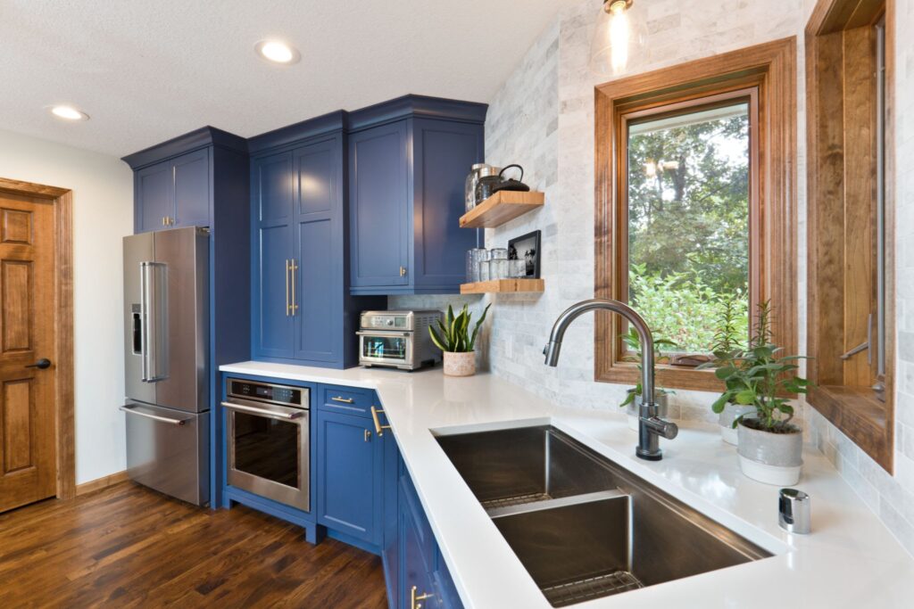 Brightly lit updated kitchen featuring freshly painted navy blue cabinets, modern hardware, stainless steel sink, and clean white countertops as an example of a high-ROI DIY weekend project.